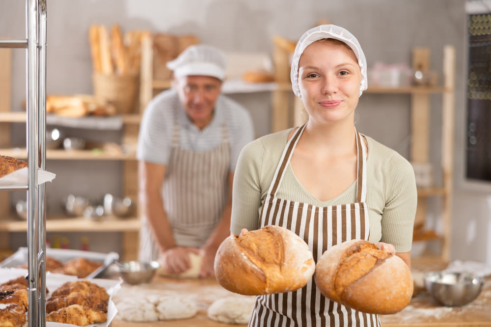 Bakery girl employee holds ready-made loafs of bread.