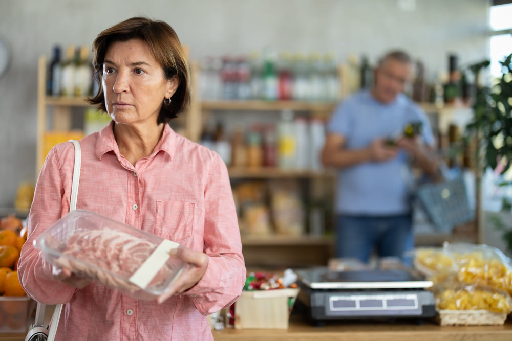 Woman chooses pork fillet, while her husband buys alcohol in supermarket