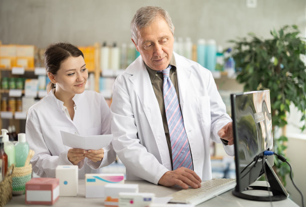 Male and female pharmacists checking prescription on computer
