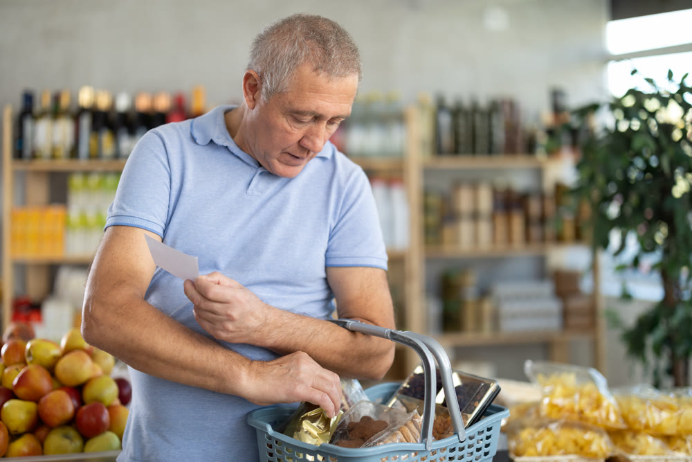 Elderly man buying groceries from shopping list in store
