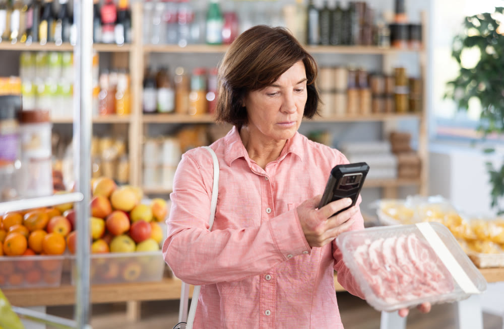 Mature woman is scanning QR on a package of pork in grocery