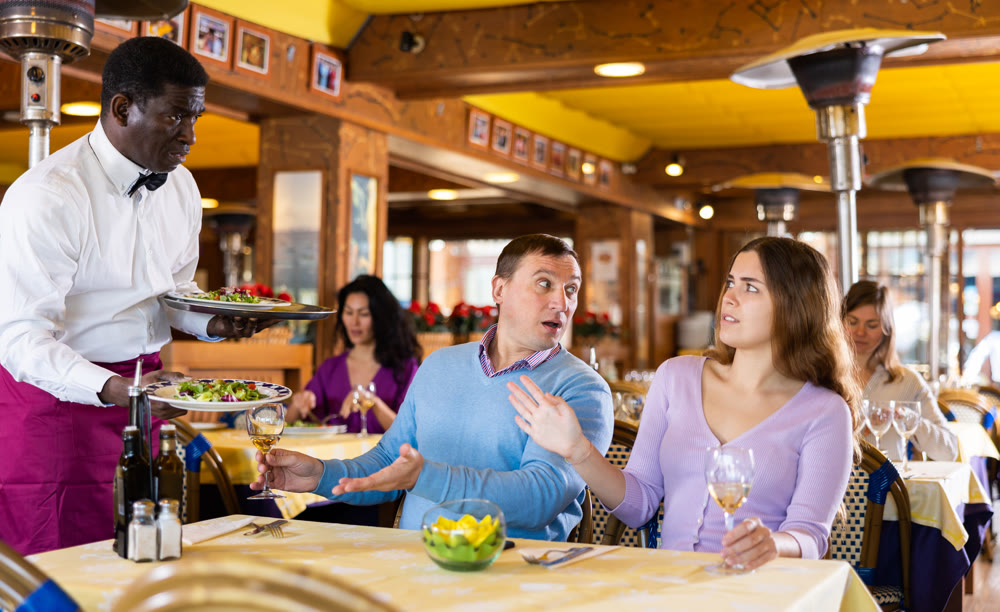 Wife and husband arguing with waiter in restaurant