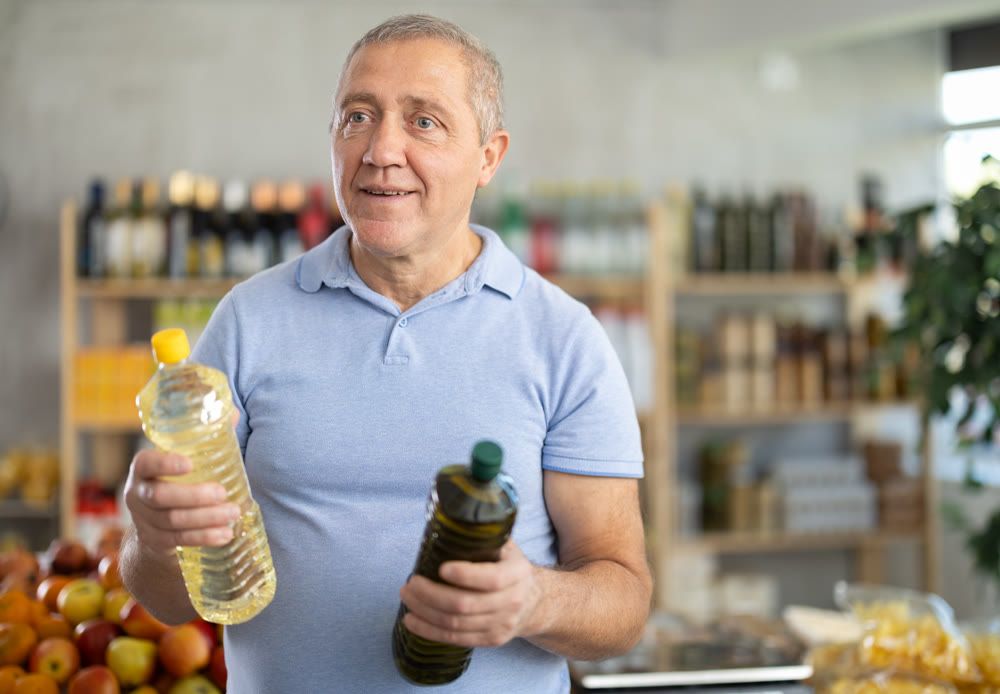 Elderly man choosing olive and sunflower oil in grocery