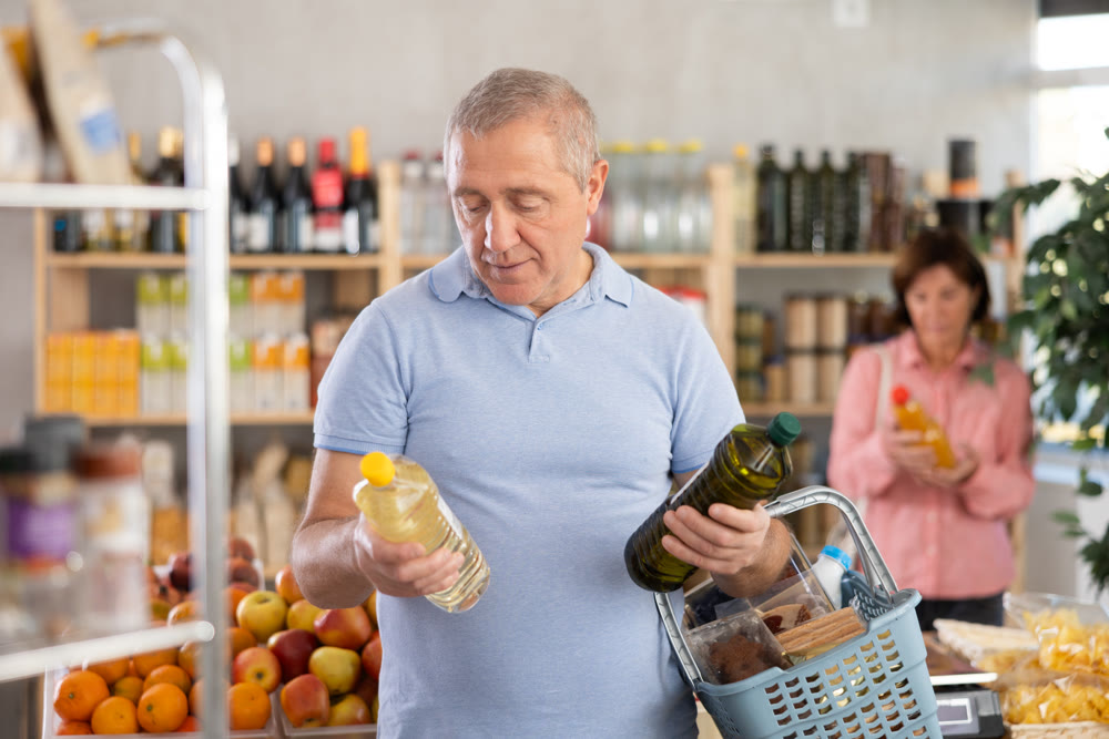 Elderly man choosing olive and sunflower oil in grocery