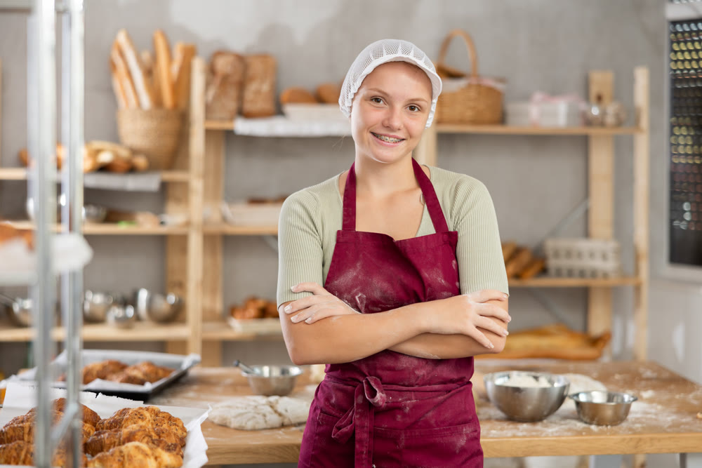 Portrait of a positive young girl baker in the kitchen of bakery