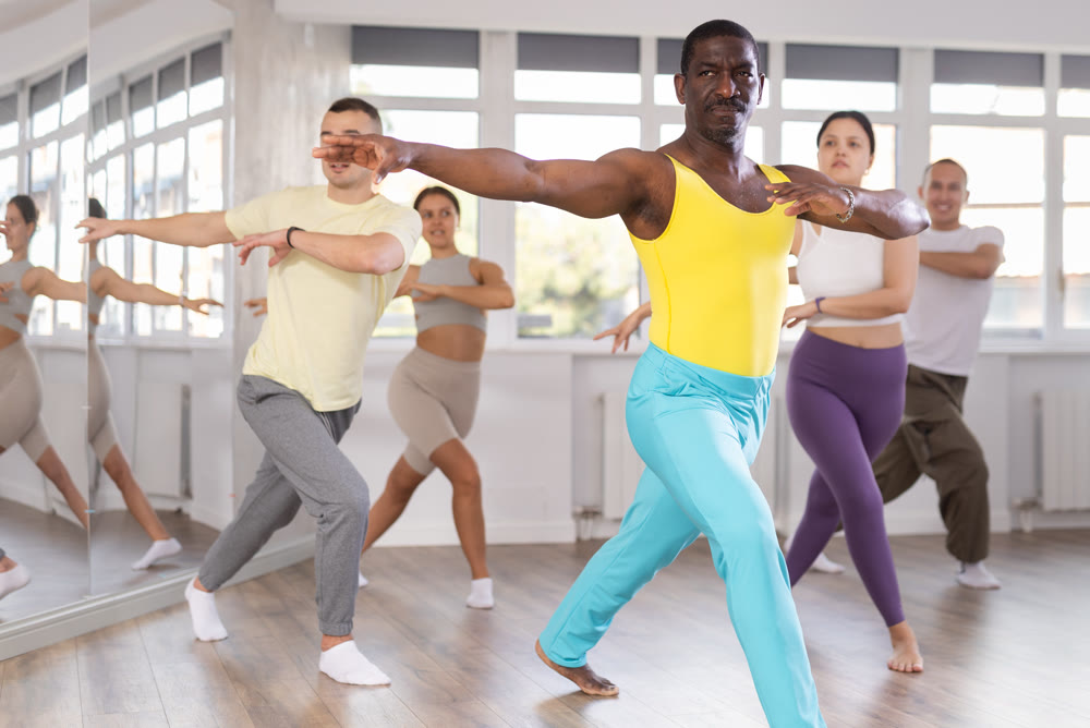 Positive African american man dancing and training movements Latin dance bachata during group class in choreography studio