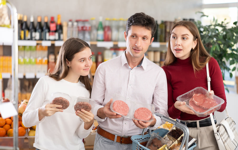 Dad, mom and daughter choose raw chilling beef entrecote and semi-finished hamburger cutlet in shop