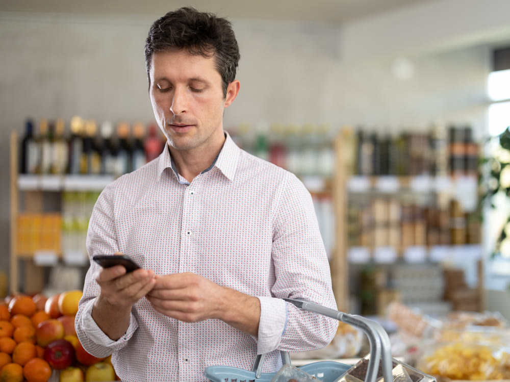 Adult man with phone choosing groceries in store