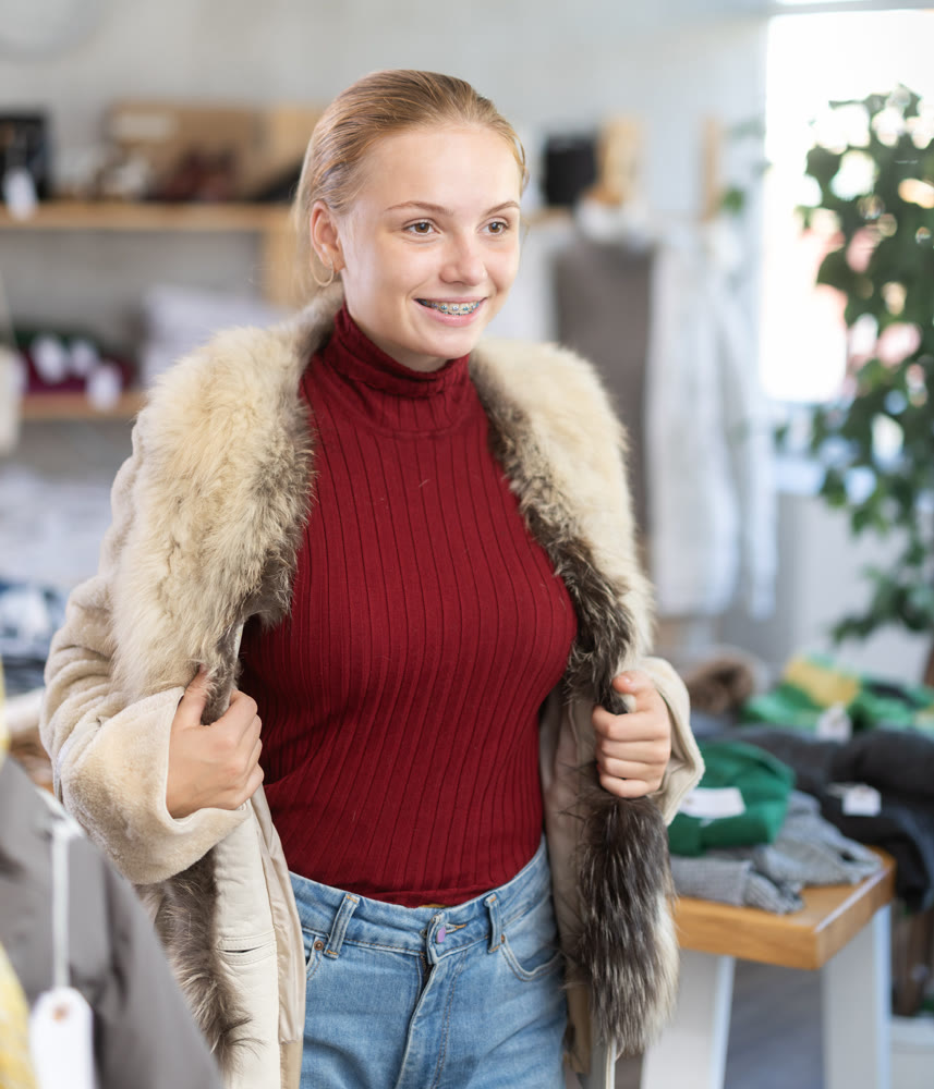 Girl try on fur coat in front of mirror