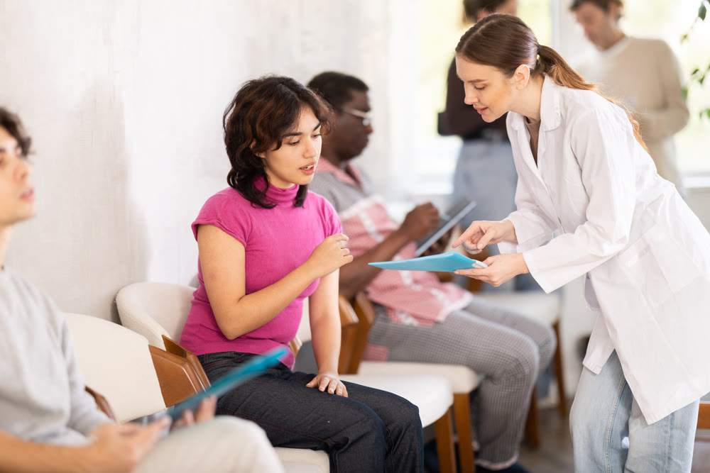 Group of people sitting in clinic queue while nurse speaking to girl