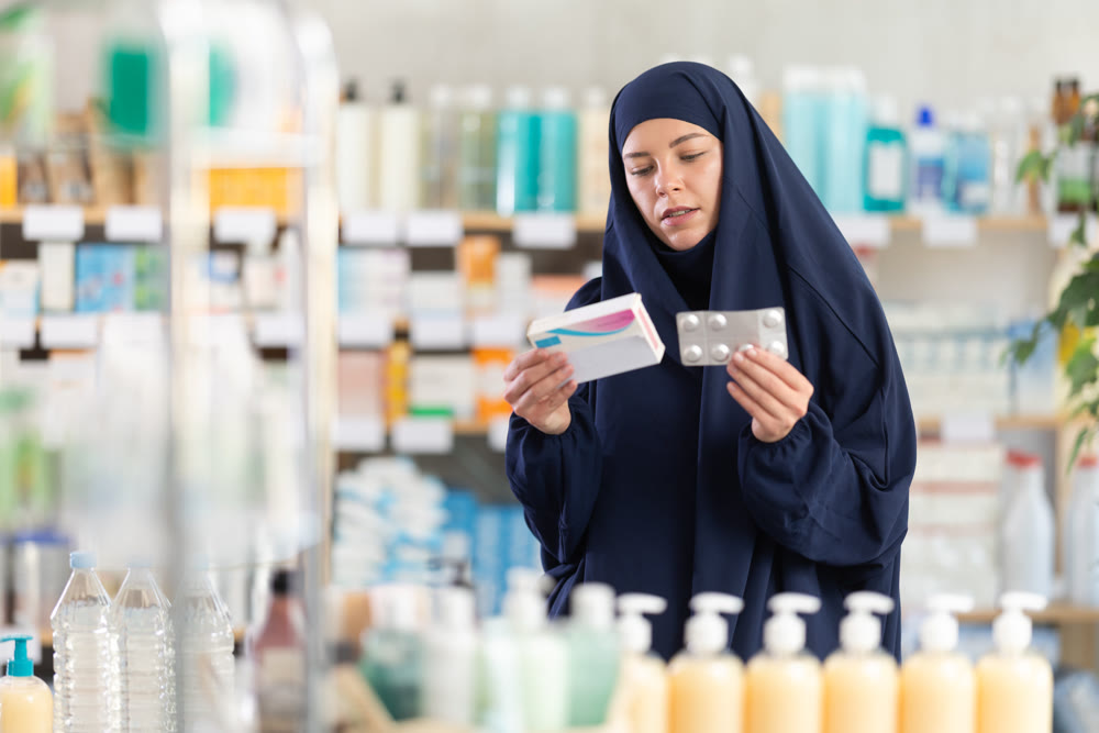 Young woman in khimar examining medicine box at pharmacy