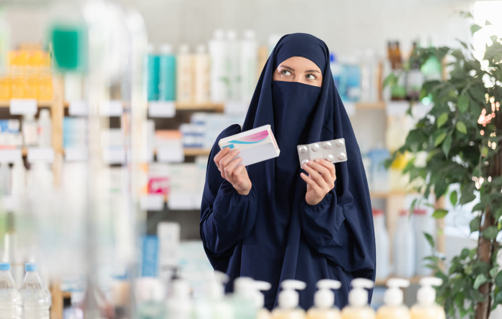 Young Muslim woman customer choosing pills in box in drugstore