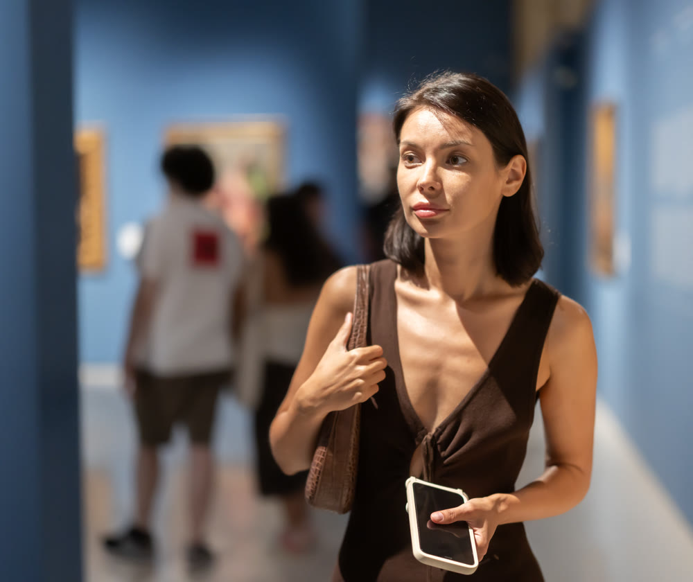 Woman visiting museum and looking at paintings in gold frames