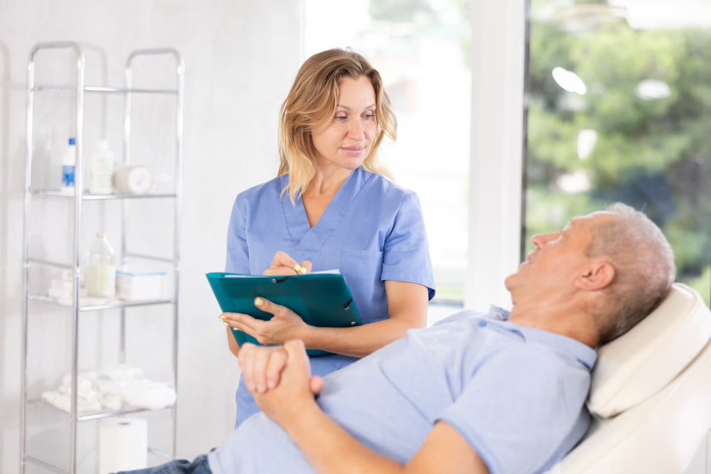 Middle-aged female doctor signing papers while talking with man patient