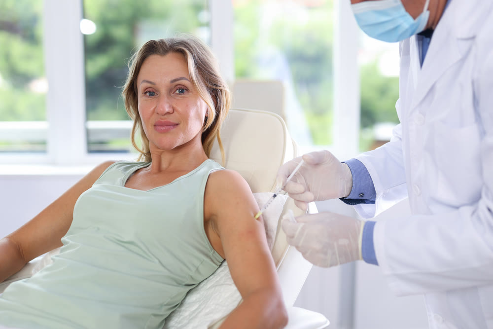 Middle-aged woman having arm injection lying on clinical chair