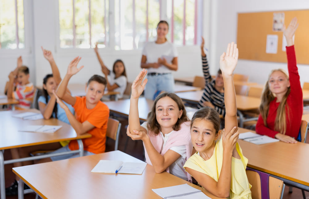 Group of school pupils raise their hands up in classroom during lesson in school