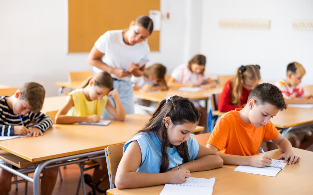 Preteen pupils studying in classroom with female teacher