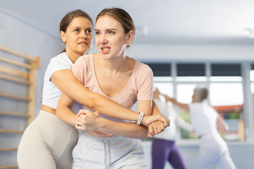 Woman trying to break free of rear grab, striking solar plexus with elbow during self-defense course
