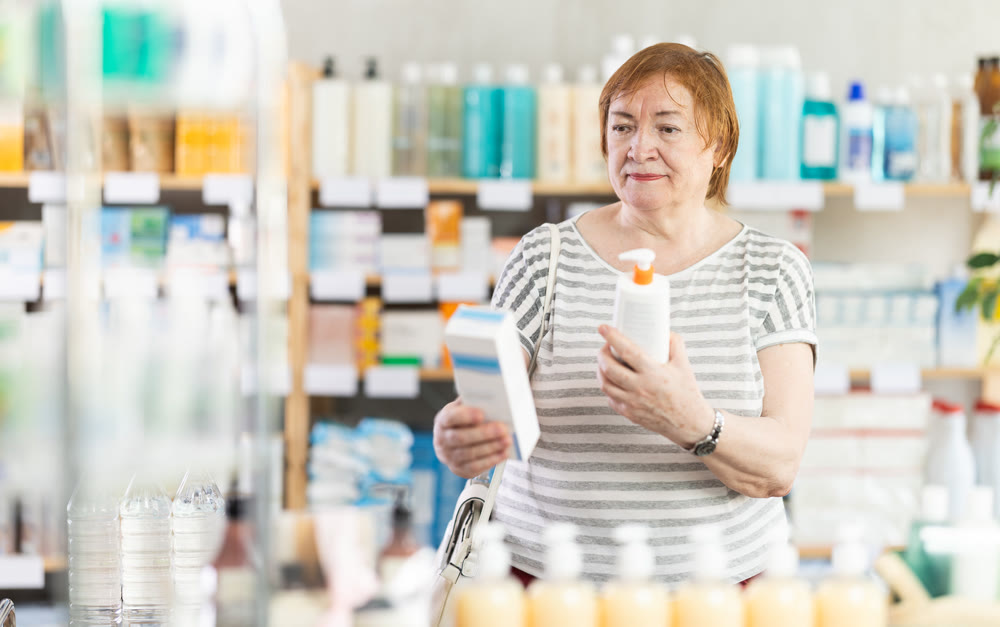 Mature female buyer choosing skin cream at drugstore