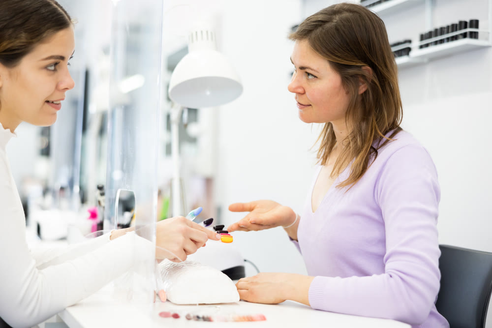 Woman manicurist offering young client to choose color of nail polishes