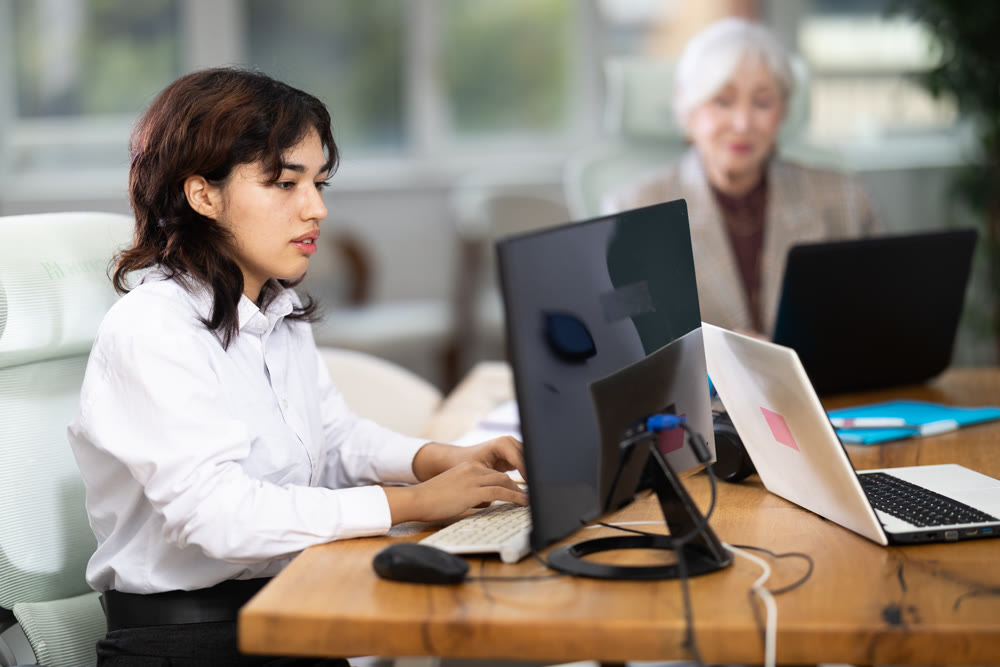 Young woman sitting at desk and typing on laptop in modern office