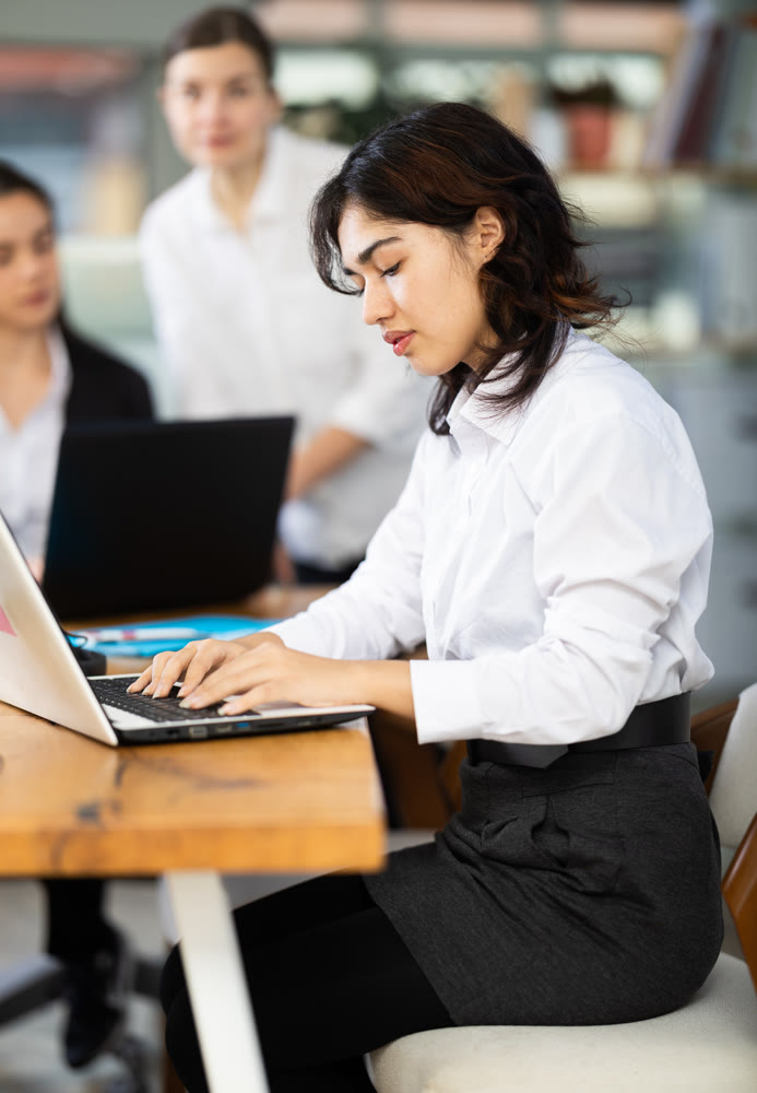 Young woman works on laptop with female colleagues