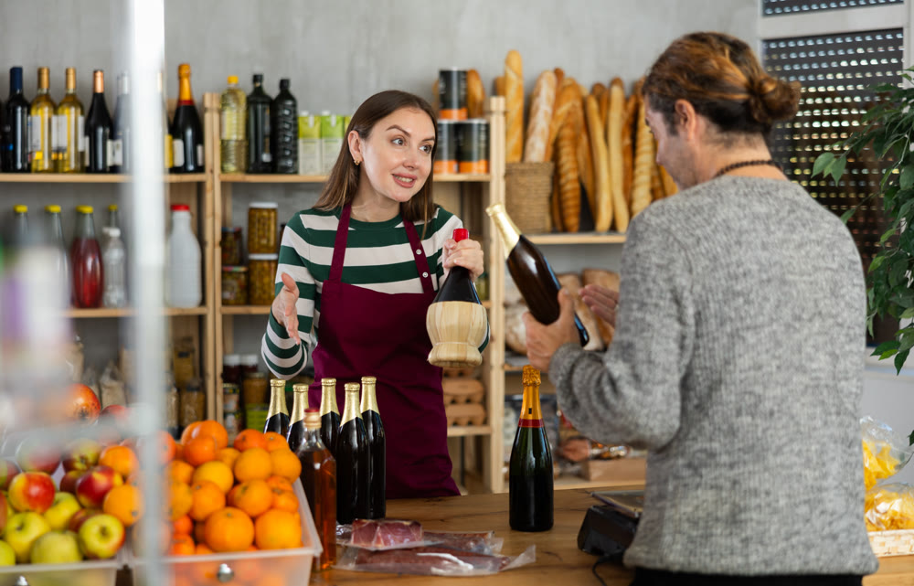 Female shop assistant offering alcoholic drink to customer in grocery store