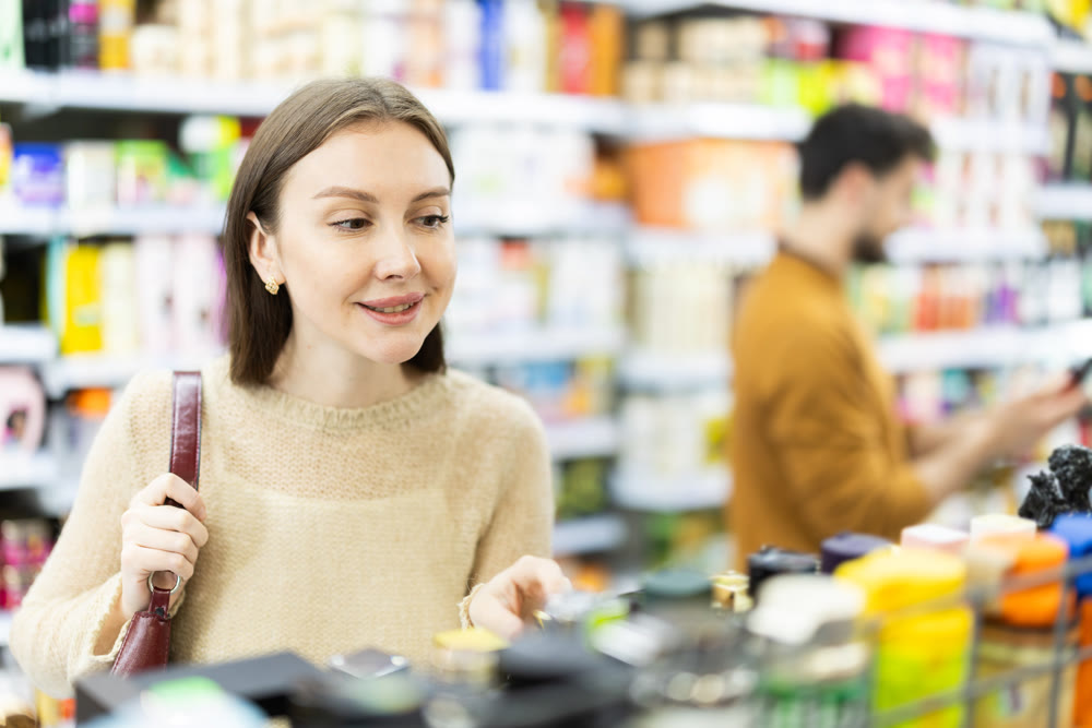 Positive woman buyers chooses shampoo or shower gel in household chemicals store