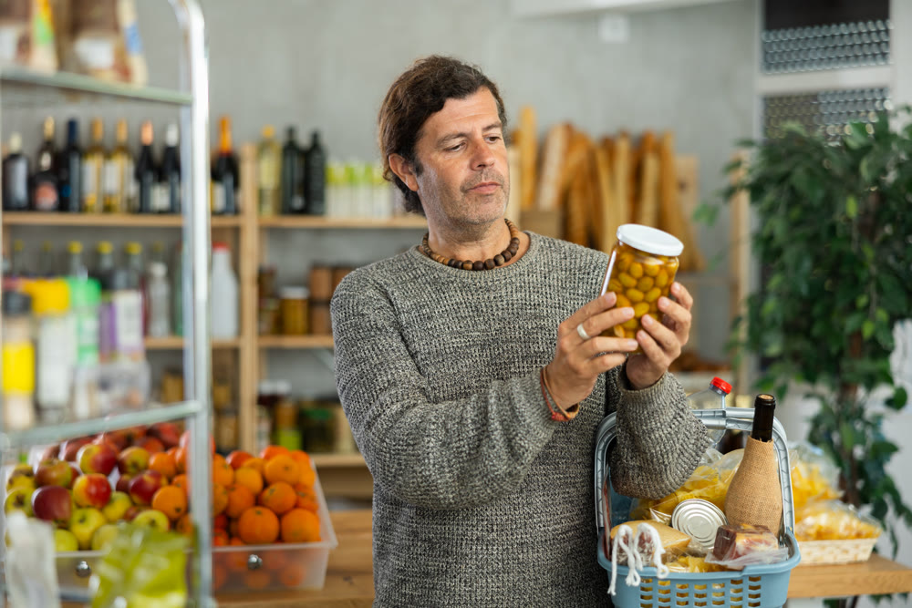 Thoughtful man choosing marinated olives in grocery store