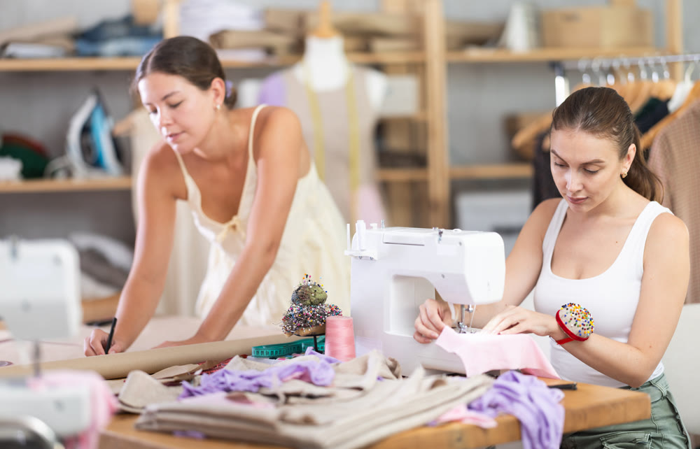 fashion designer draws patterns of dresses next to a seamstress