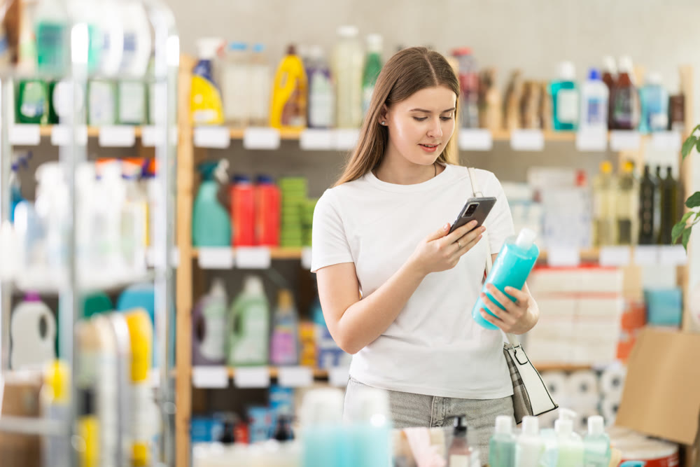 Checking expiration date of shampoo or shower gel - female shopper scans QR code on label of shampoo using smartphone