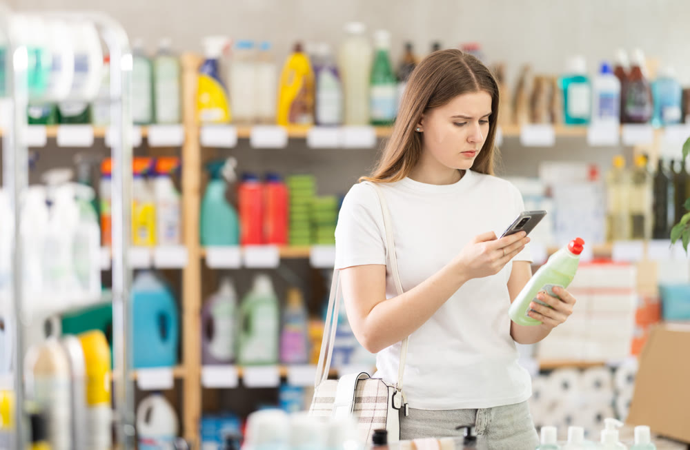 Young fmale shopper scans QR code on label of dishwashing for windows using smartphone