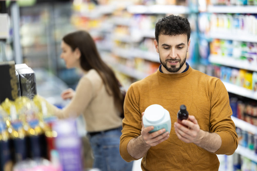 Young man choosing body and hair care products in supermarket