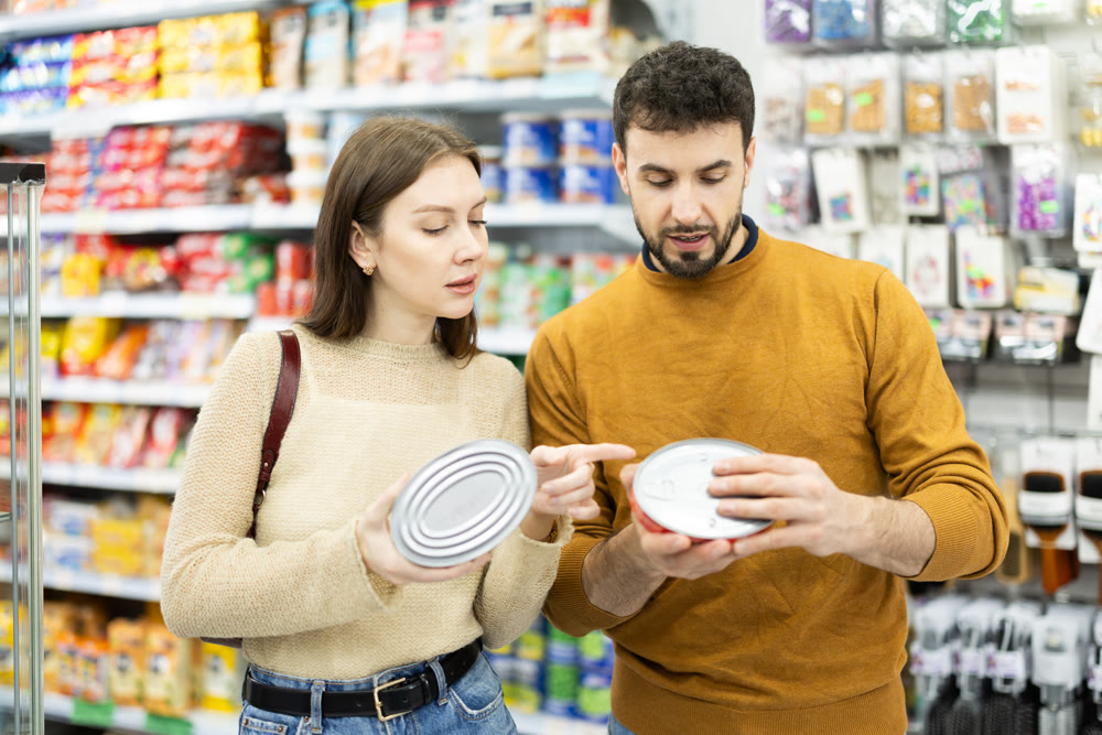 Couple of shoppers are choosing canned fish in food store