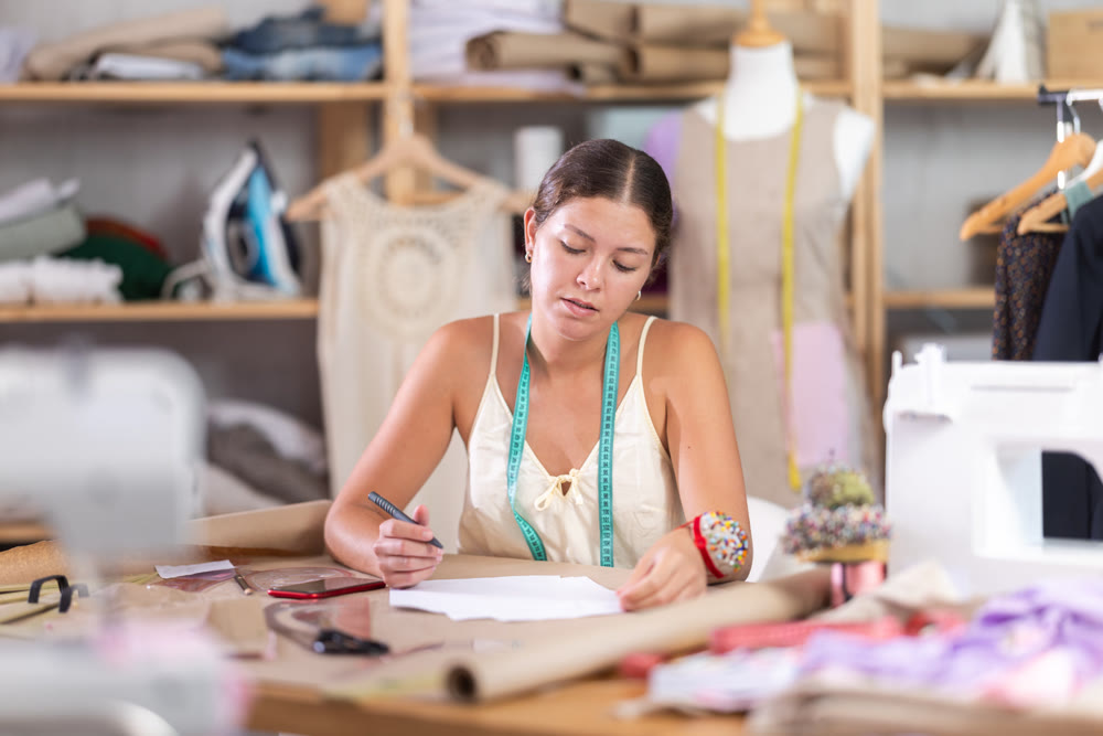 Young tailoress engaged in paperwork in sewing workshop
