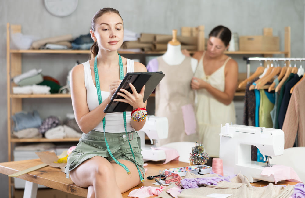 dressmaker draws a sketch in the workshop with a seamstress in the background