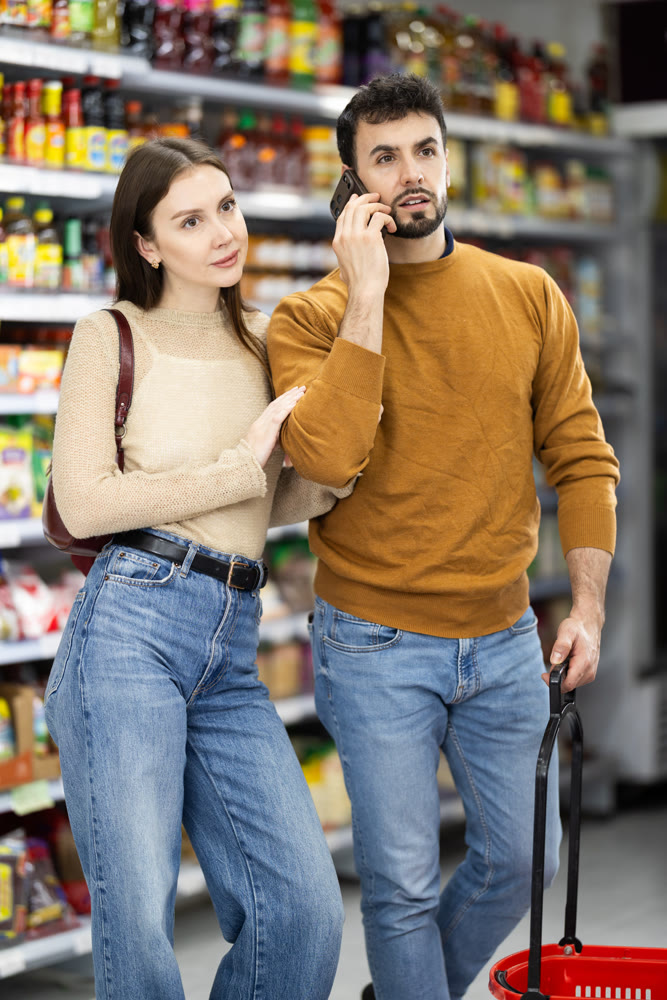 Young couple shopping for groceries man talks on phone