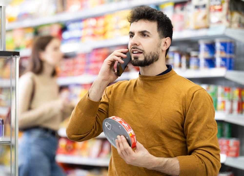 Young man choosing canned goods while talking on phone