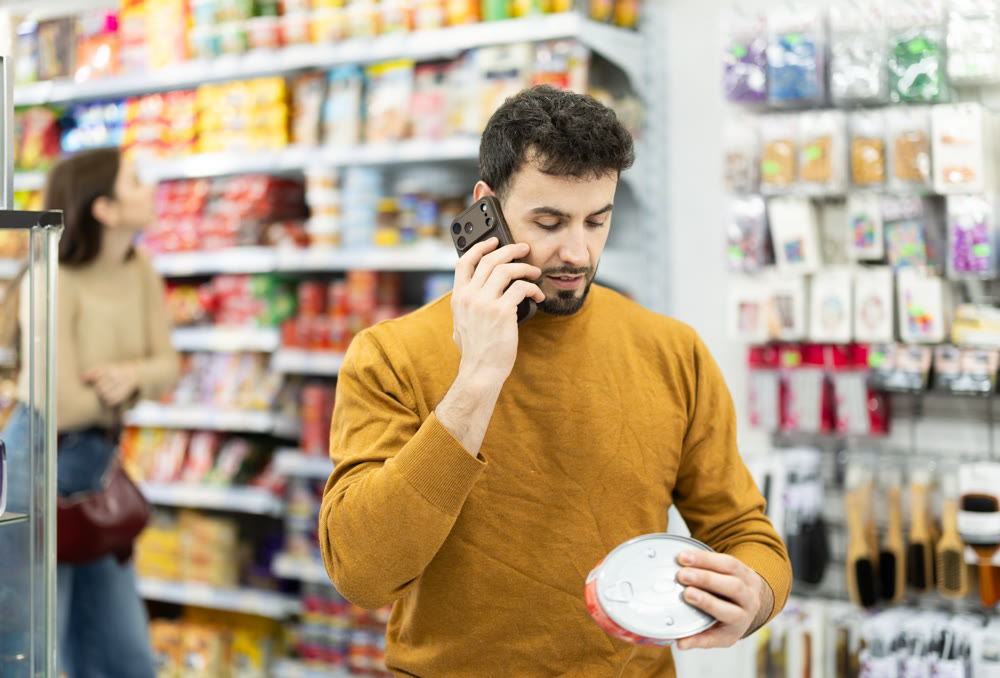 In store, man examines tin can product and talks on phone, advises on purchase.
