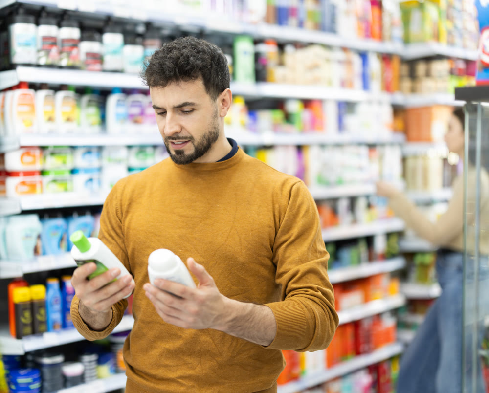 Young man choosing body and hair care products in supermarket