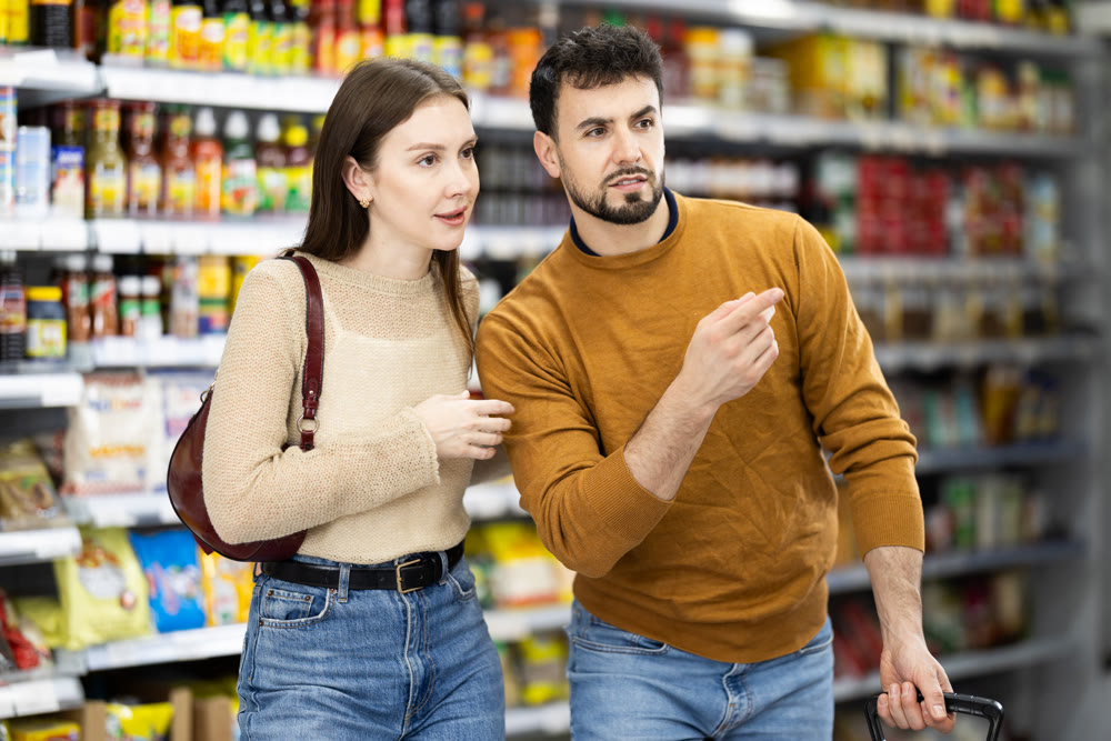 In food store, couple buyer looking for something on shelf of showcase