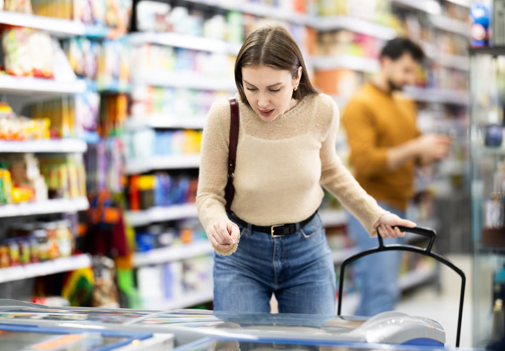 Woman standing near refrigerated display cases choosing frozen food in supermarket