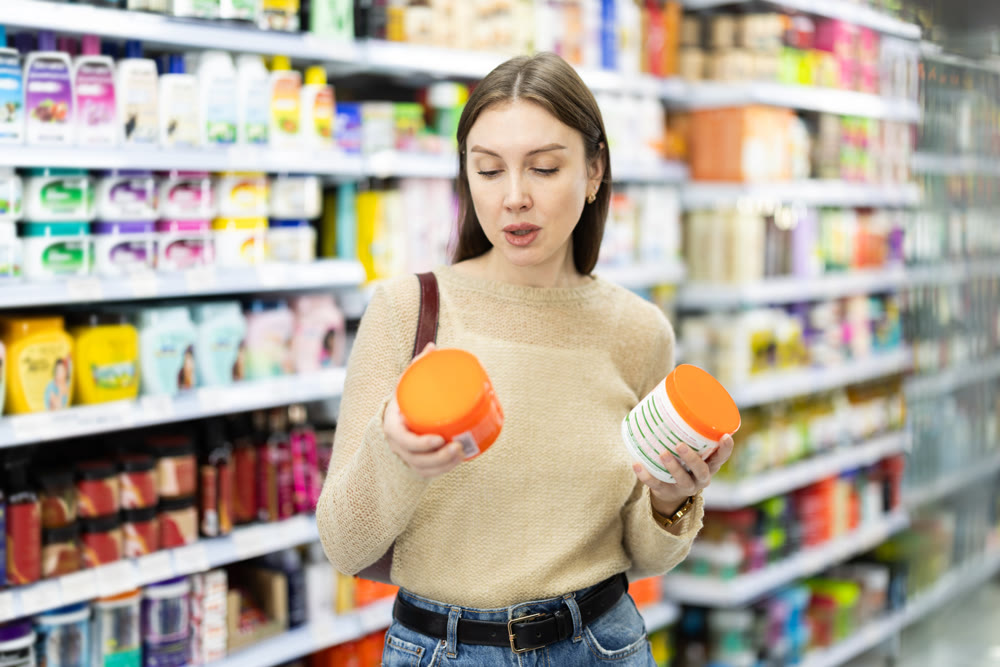 Positive woman buyers chooses shampoo or shower gel in household chemicals store