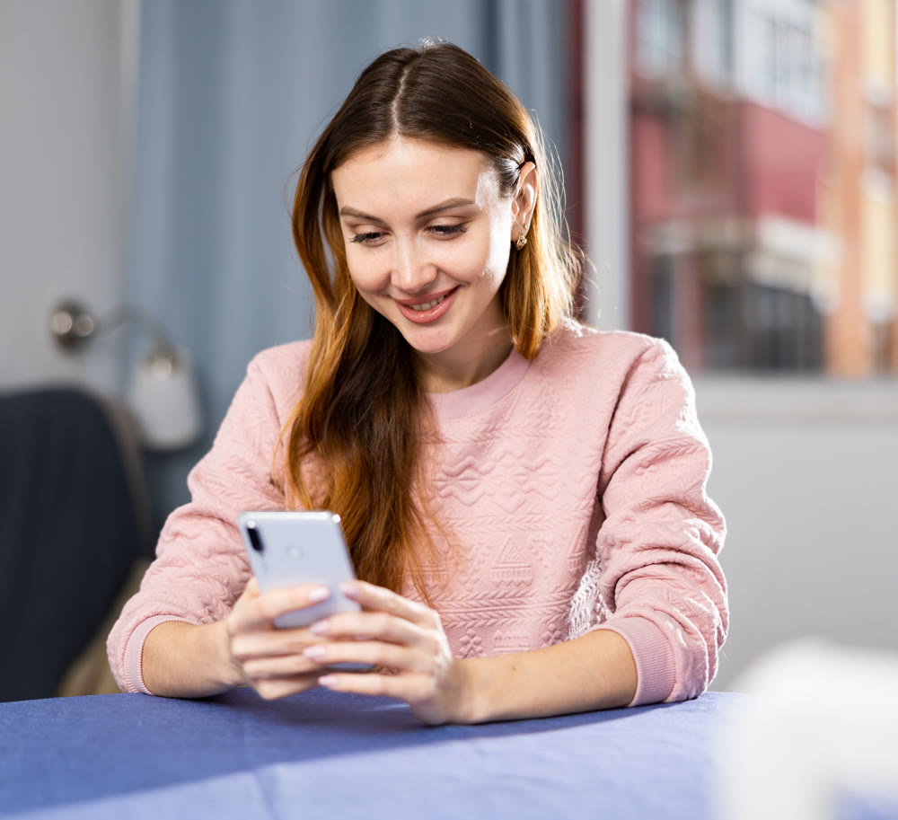 Portrait of pleased joyful woman with smartphone in her hands at the table at home