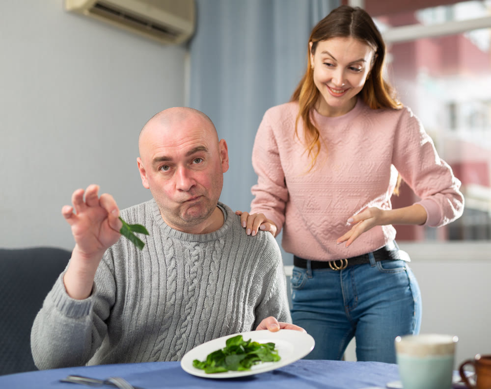 Portrait of a disgruntled man, to whom a young woman brought a plate of spinach