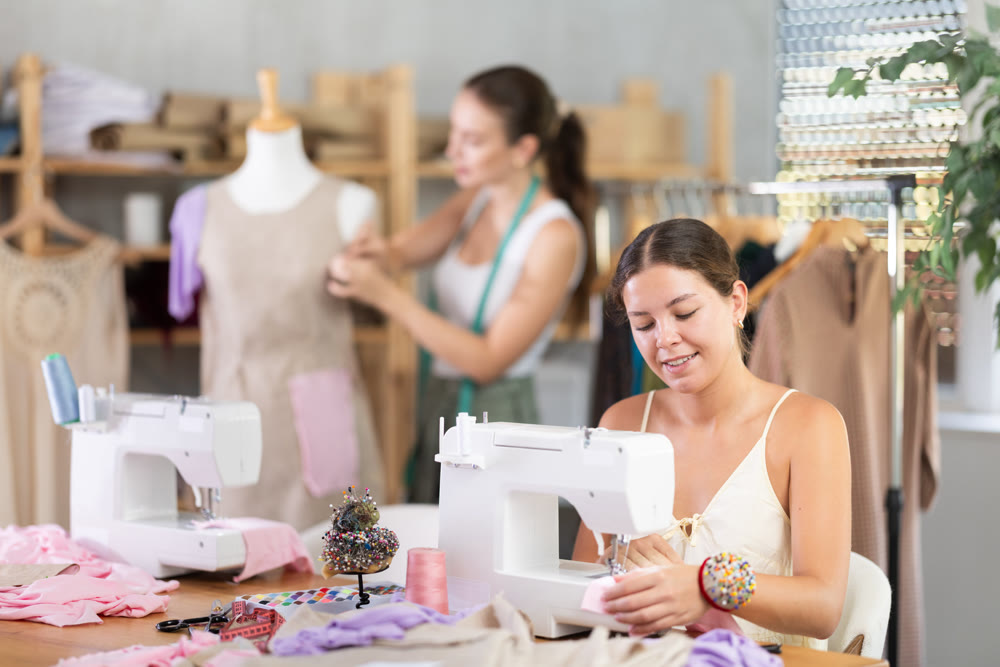 Woman seamstress operating by sewing machine. Assistant work with mannequin in background