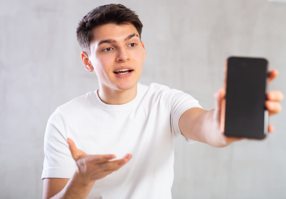 Enthusiastic young man showing screen of mobile phone excitedly
