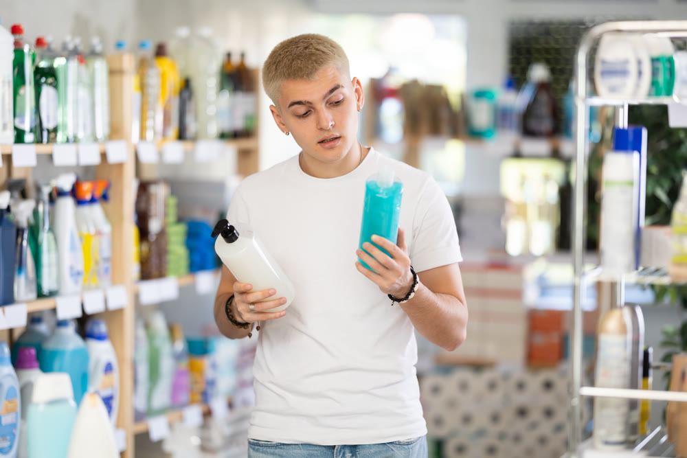 Guy buyer chooses shampoo or shower gel in household goods department of supermarket