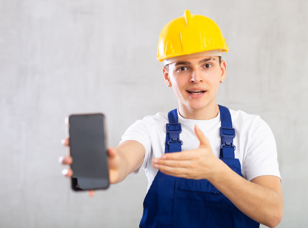 Enthusiastic young worker showing screen of mobile phone excitedly