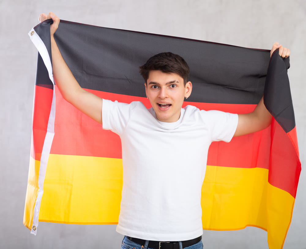Excited, active male spectator holds national flag of Germany in hands and chants popular slogan